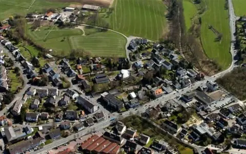 Luftaufnahme eines Dorfes mit Häusern, Straßen und Feldern.