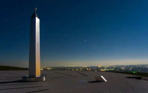 Die Sonnenuhr in Herten ragt unter einem sternenklaren Nachthimmel empor. Ein glänzender Obelisk wirft lange Schatten auf die gepflasterte Fläche.