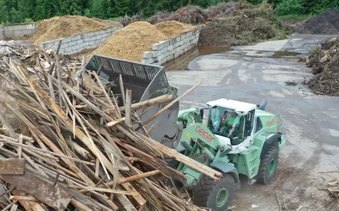 Radlader sammelt Holzreste für die Wiederverwertung. Große Haufen von recycelten Materialien sind im Hintergrund zu sehen.
