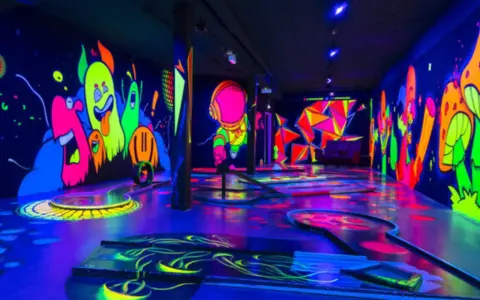 Ein leuchtendes Indoor-Minigolf-Paradies mit Neon-Wänden, die bunte Monster und Pilze zeigen.