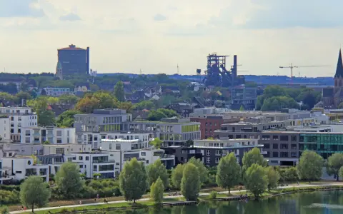 Moderne Wohngebäude am Wasser, im Hintergrund Industriedenkmäler und eine Kirche. Der Wohnungsmarkt Dortmund zeigt sich hier von seiner modernen Seite.