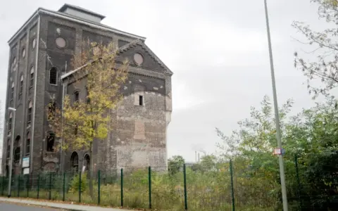 Ein verlassener Malakowturm aus dunklem Backstein, umgeben von Bäumen im Herbstlaub.