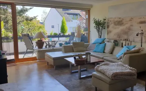 Gemütliches Wohnzimmer mit Ledercouch, Blick auf Balkon und Garten. Ein schönes Zuhause, das die Immobilienpreise in Ratingen widerspiegelt.
