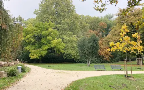 Herbstliche Farben im Schlosspark Herten. Ein Kiesweg führt durch den Park, vorbei an Bänken und Bäumen in bunten Herbsttönen.