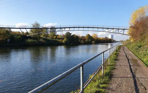 Ein Radweg am Rhein-Herne-Kanal führt unter einer modernen Brücke hindurch. Herbstlaub schmückt die Ufer.