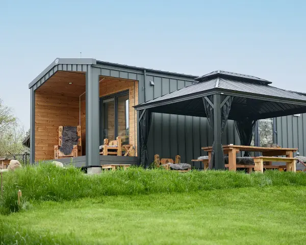 Modernes Tiny House mit Holzveranda, Sitzmöbeln und Pavillon. Ein Beispiel für die Tiny house movement, das minimalistisches Wohnen im Grünen ermöglicht.