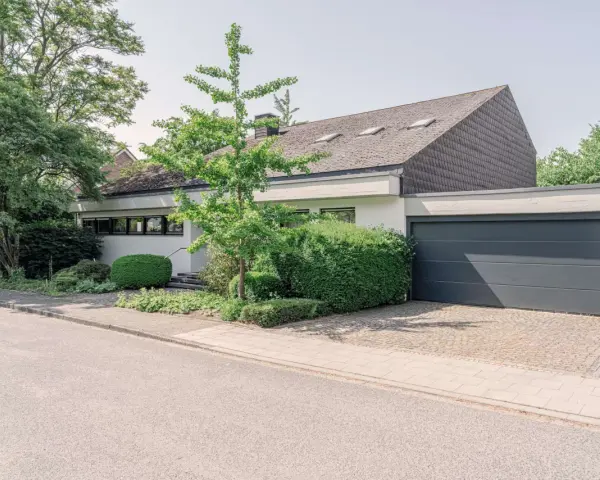 Modernes Haus mit Garage und gepflegtem Garten. Eine Einliegerwohnung könnte hier Vorteile wie zusätzliche Mieteinnahmen bieten, aber auch Nachteile wie Lärm oder Privatsphäreverlust mit sich bringen.