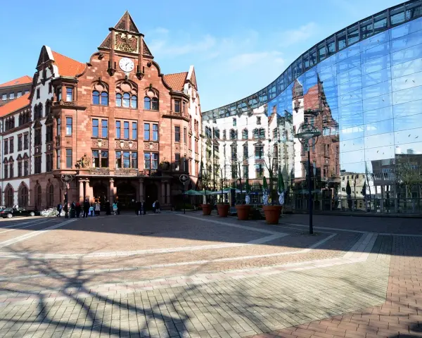 Historisches Gebäude und moderne Glasfassade spiegeln sich auf dem Platz. Hier könnte man sich über den Mietspiegel Dortmund informieren.