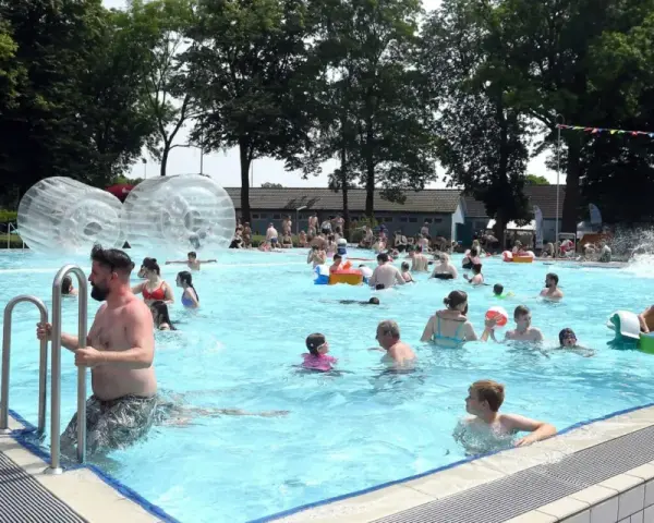 Menschen genießen einen sonnigen Tag im Parkbad Nord. Kinder planschen, rutschen und spielen in den Wasserbällen.