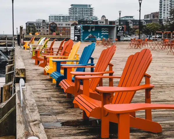 Reihe bunter Adirondack-Stühle am Kai. Die Haard ist leer, aber die Stühle laden zum Verweilen ein.