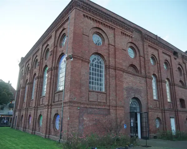 Das imposante Backsteingebäude der Zeche Scherlbeck mit seinen vielen Rund- und Bogenfenstern, einige davon bunt beleuchtet, strahlt historischen Charme aus.