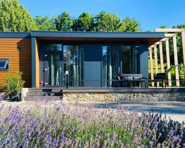 Modernes tiny house im garten der eltern, umgeben von Lavendel und Bäumen. Eine Terrasse mit Sitzmöbeln lädt zum Entspannen ein.