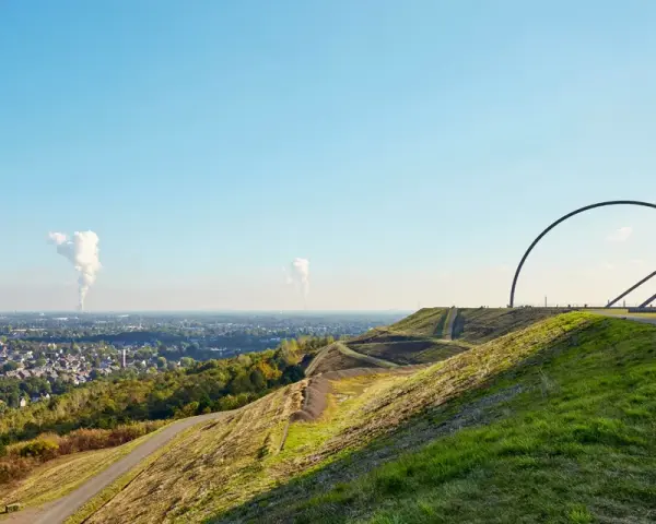 Blick über die Halde Recklinghausen mit der markanten Hängebrücke und rauchenden Schloten in der Ferne.