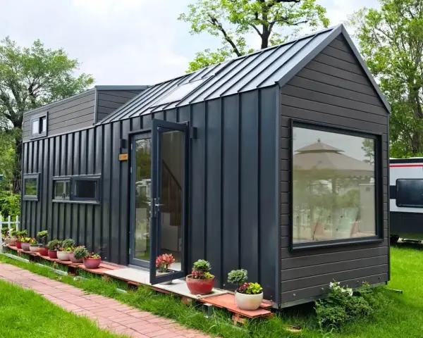 Modernes Tiny House als Anbau mit dunkler Fassade, Glasfront und vielen Pflanzen.