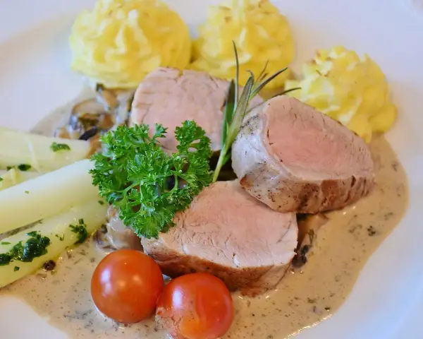 Zartes Schweinefilet mit Kartoffelröschen, Spargel und einer cremigen Sauce, serviert wie in einer alten Dorfbrennerei.