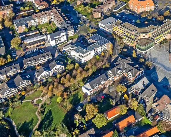 Luftaufnahme eines Wohngebiets mit Mehrfamilienhäusern und Einfamilienhäusern. Die Bäume zeigen Herbstlaub. Ein zentraler Platz ist zu sehen. Hier könnte man den Mietspiegel Voerde studieren.