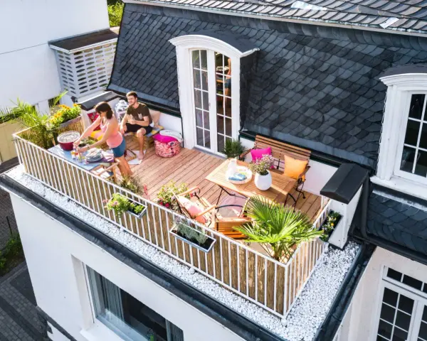 Ein Paar genießt den Sommer auf einem Balkon mit Holz-Bodenbelag, ideal für eine Mietwohnung. Grillen und Entspannen stehen im Vordergrund.
