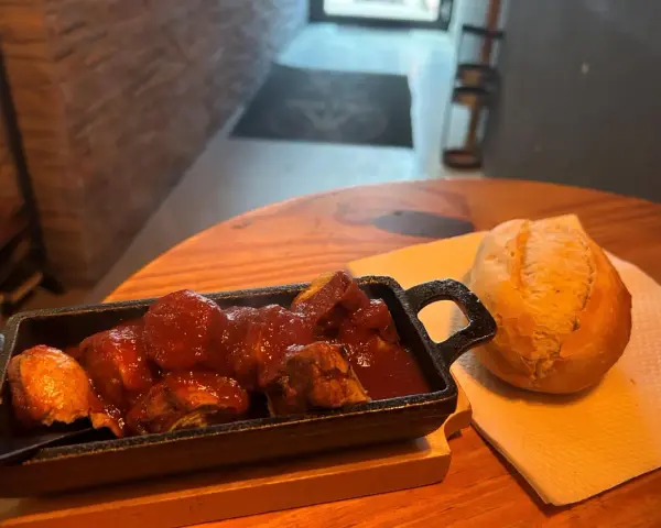 Herzhafte Steiger Wurst in Tomatensoße mit einem Brötchen auf einem Holztisch.