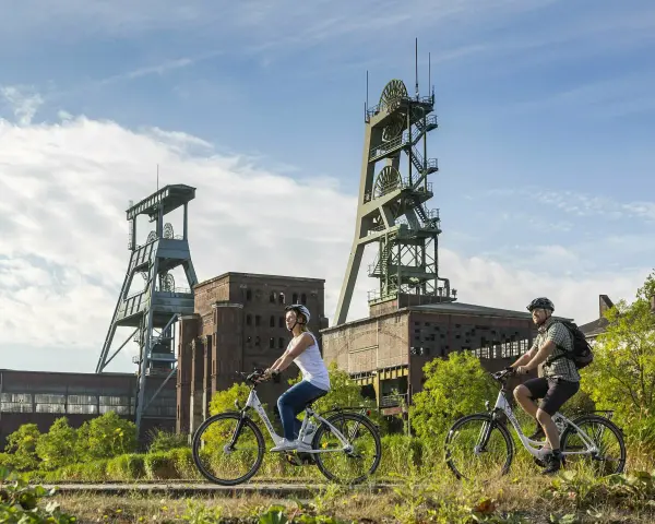 Ein Paar genießt eine Fahrradtour in Recklinghausen, vorbei an alten Fördertürmen und Industriegebäuden.