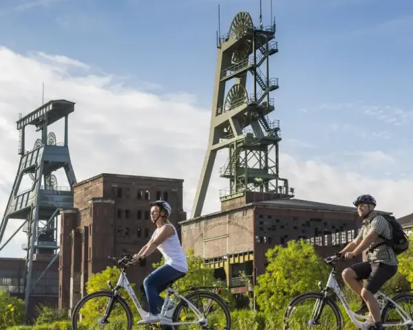 Zwei Radfahrer genießen die Aussicht auf die beeindruckenden Fördertürme der Zeche Ewald, ein Symbol für Industriegeschichte und neuen Freizeitwert.