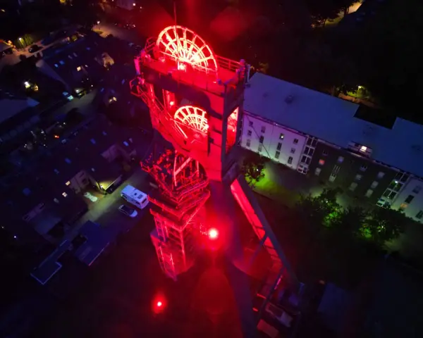 Der beleuchtete Förderturm des Erzschacht Marl erstrahlt in rotem Licht.