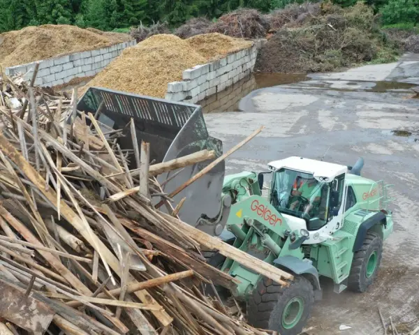 Radlader sammelt Holzreste für die Wiederverwertung. Große Haufen von recycelten Materialien sind im Hintergrund zu sehen.