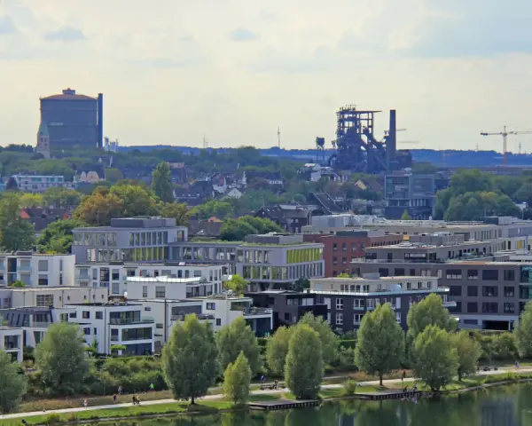 Moderne Wohngebäude am Wasser, im Hintergrund Industriedenkmäler und eine Kirche. Der Wohnungsmarkt Dortmund zeigt sich hier von seiner modernen Seite.