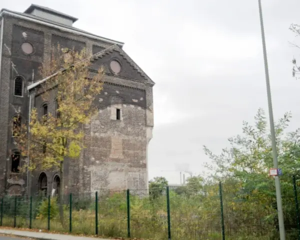 Ein verlassener Malakowturm aus dunklem Backstein, umgeben von Bäumen im Herbstlaub.