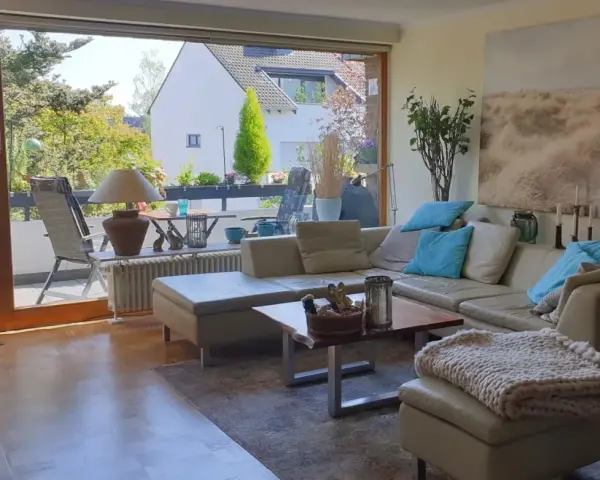 Gemütliches Wohnzimmer mit Ledercouch, Blick auf Balkon und Garten. Ein schönes Zuhause, das die Immobilienpreise in Ratingen widerspiegelt.