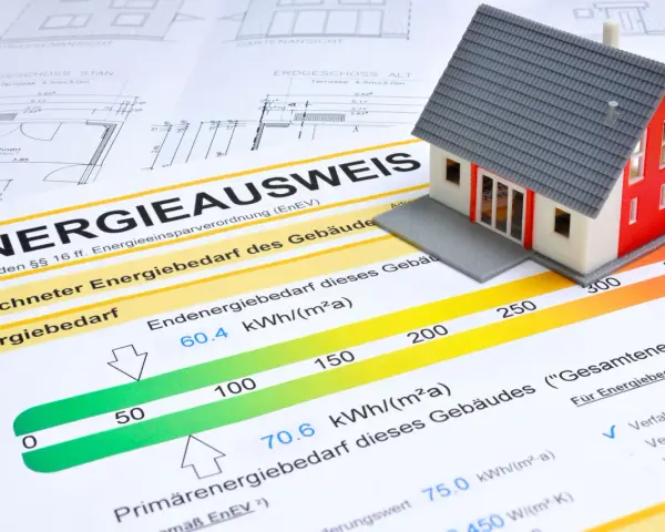 Modellhaus auf einem Energieausweis (Verbrauchsausweis oder Bedarfsausweis). Der Ausweis zeigt den Energiebedarf eines Gebäudes mit einer Skala von grün bis rot.