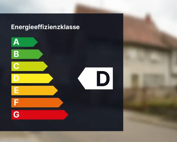 Energieeffizienzklasse D auf einem dunklen Hintergrund. Das Haus im Hintergrund hat eine braune Ziegeldach.