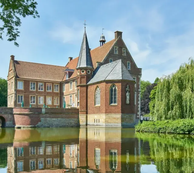 Wasserschloss in Haltern am See, umgeben von einem Wassergraben und üppiger Vegetation.