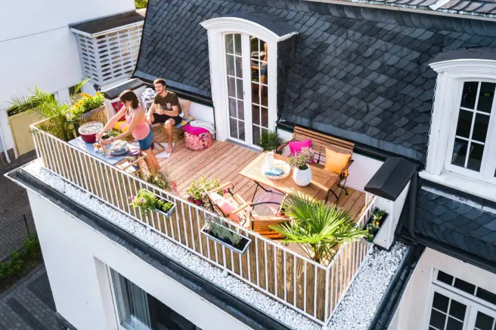 Ein Paar genießt den Sommer auf einem Balkon mit Holz-Bodenbelag, ideal für eine Mietwohnung. Grillen und Entspannen stehen im Vordergrund.