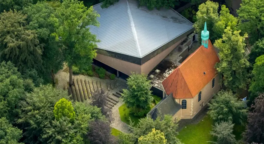 Luftaufnahme von Annaberg Haltern: Ein Gotteshaus mit rotem Ziegeldach und grüner Turmspitze, daneben ein moderner Bau mit Pyramiden-Dach, umgeben von üppigem Grün.