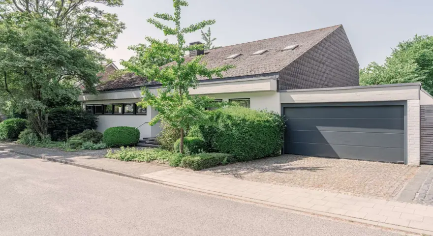 Modernes Haus mit Garage und gepflegtem Garten. Eine Einliegerwohnung könnte hier Vorteile wie zusätzliche Mieteinnahmen bieten, aber auch Nachteile wie Lärm oder Privatsphäreverlust mit sich bringen.