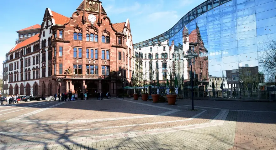 Historisches Gebäude und moderne Glasfassade spiegeln sich auf dem Platz. Hier könnte man sich über den Mietspiegel Dortmund informieren.