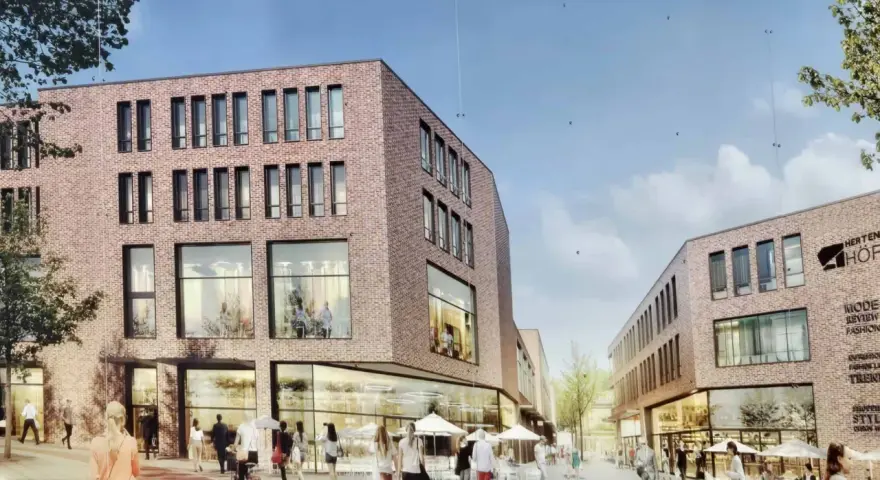 Belebtes Treiben in der Herten Innenstadt: Menschen flanieren vor modernen Backsteingebäuden mit großen Fensterfronten und Cafés.