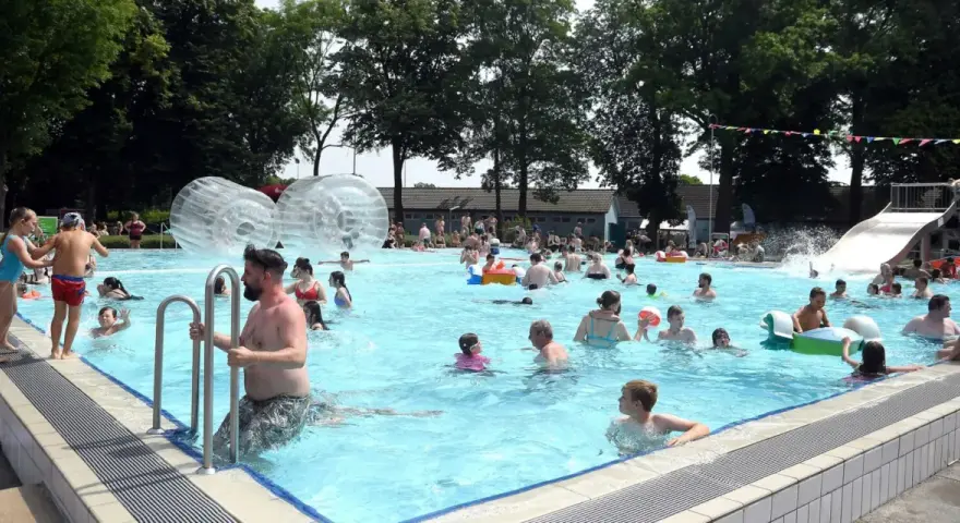 Menschen genießen einen sonnigen Tag im Parkbad Nord. Kinder planschen, rutschen und spielen in den Wasserbällen.
