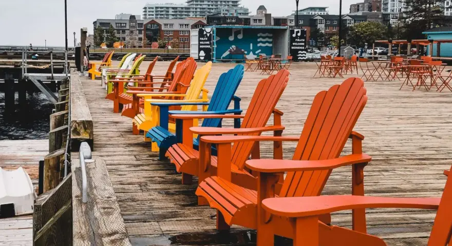 Reihe bunter Adirondack-Stühle am Kai. Die Haard ist leer, aber die Stühle laden zum Verweilen ein.