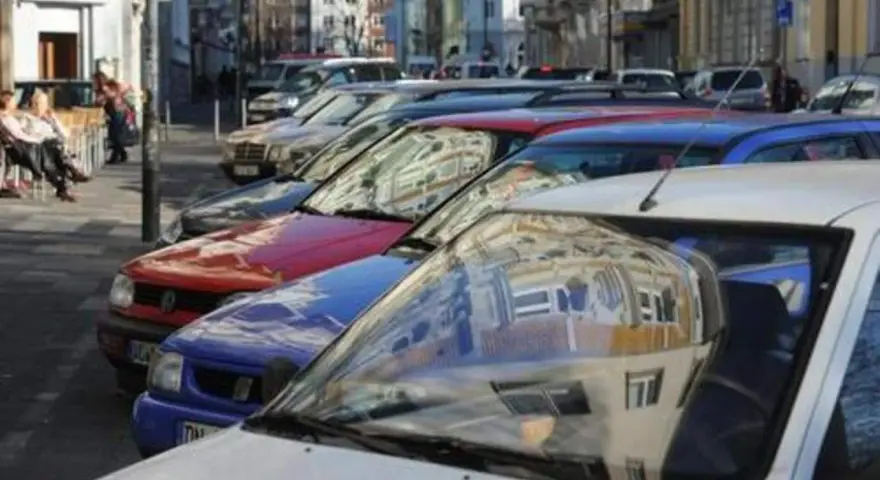 Autos parken in einer Reihe im Frankenberger Viertel Aachen. Menschen sitzen an einem Tisch im Hintergrund.