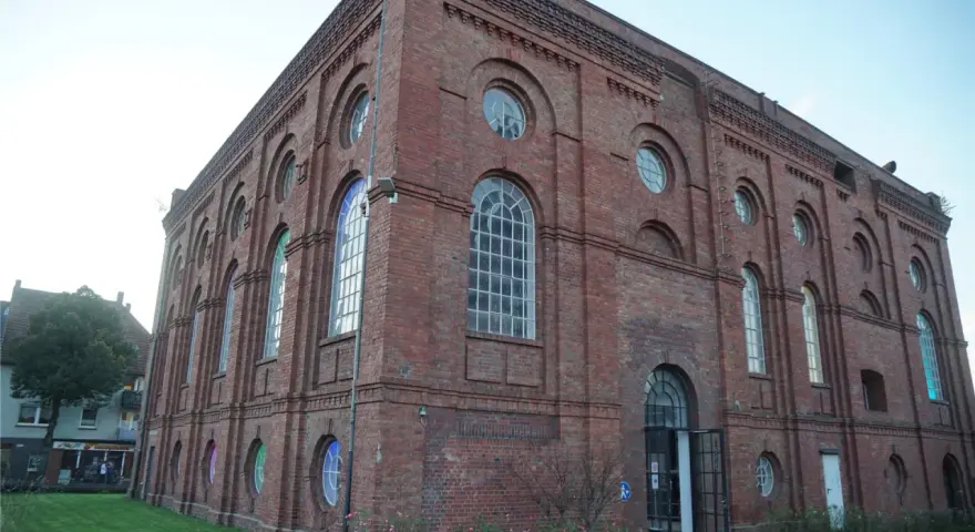 Das imposante Backsteingebäude der Zeche Scherlbeck mit seinen vielen Rund- und Bogenfenstern, einige davon bunt beleuchtet, strahlt historischen Charme aus.