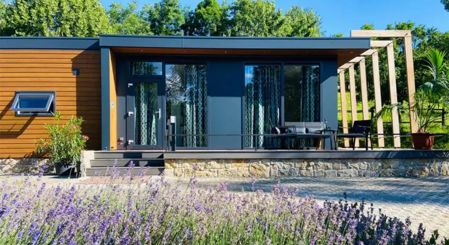 Modernes tiny house im garten der eltern, umgeben von Lavendel und Bäumen. Eine Terrasse mit Sitzmöbeln lädt zum Entspannen ein.