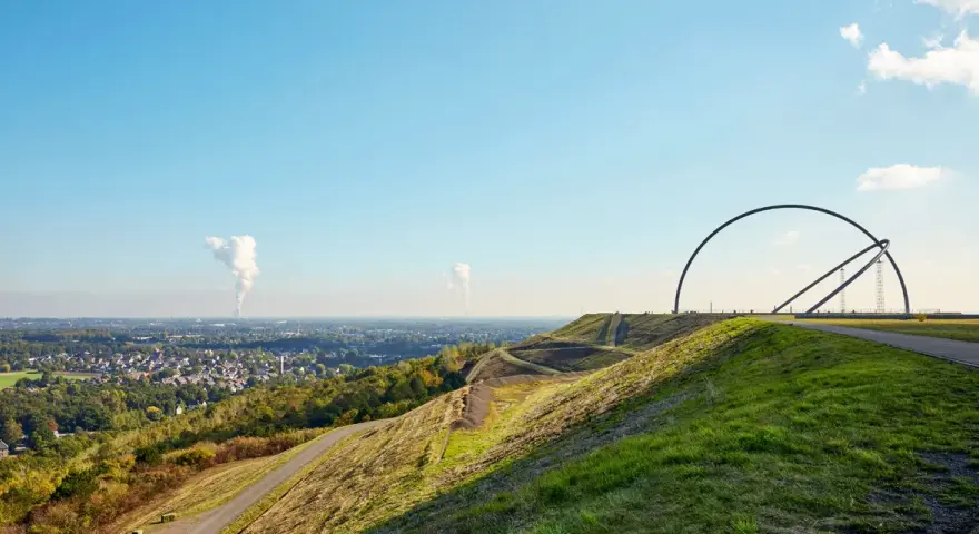 Blick über die Halde Recklinghausen mit der markanten Hängebrücke und rauchenden Schloten in der Ferne.