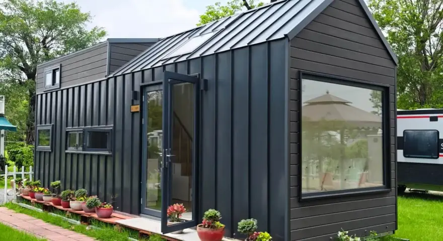 Modernes Tiny House als Anbau mit dunkler Fassade, Glasfront und vielen Pflanzen.