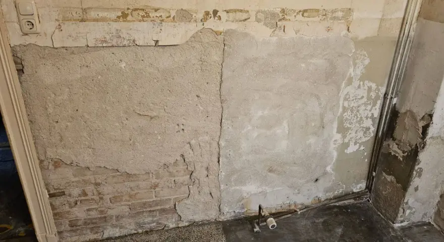 Abblätternder Putz an einer Wand mit freiliegenden Ziegeln und einer Steckdose. Vorsicht bei der Renovierung, um **asbest erkennen** zu können.