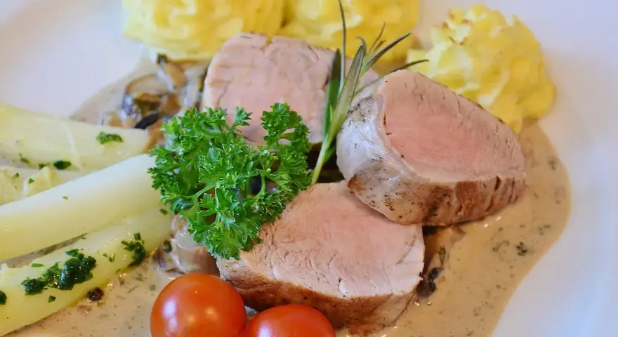 Zartes Schweinefilet mit Kartoffelröschen, Spargel und einer cremigen Sauce, serviert wie in einer alten Dorfbrennerei.