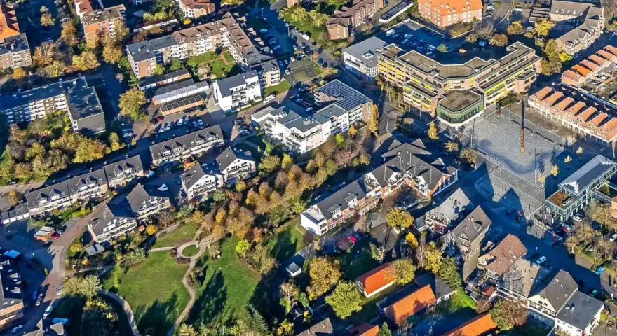 Luftaufnahme eines Wohngebiets mit Mehrfamilienhäusern und Einfamilienhäusern. Die Bäume zeigen Herbstlaub. Ein zentraler Platz ist zu sehen. Hier könnte man den Mietspiegel Voerde studieren.