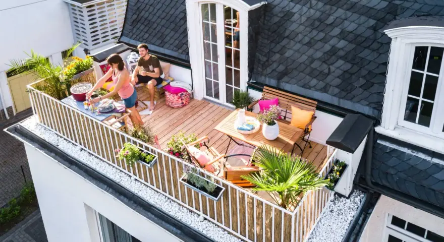Ein Paar genießt den Sommer auf einem Balkon mit Holz-Bodenbelag, ideal für eine Mietwohnung. Grillen und Entspannen stehen im Vordergrund.