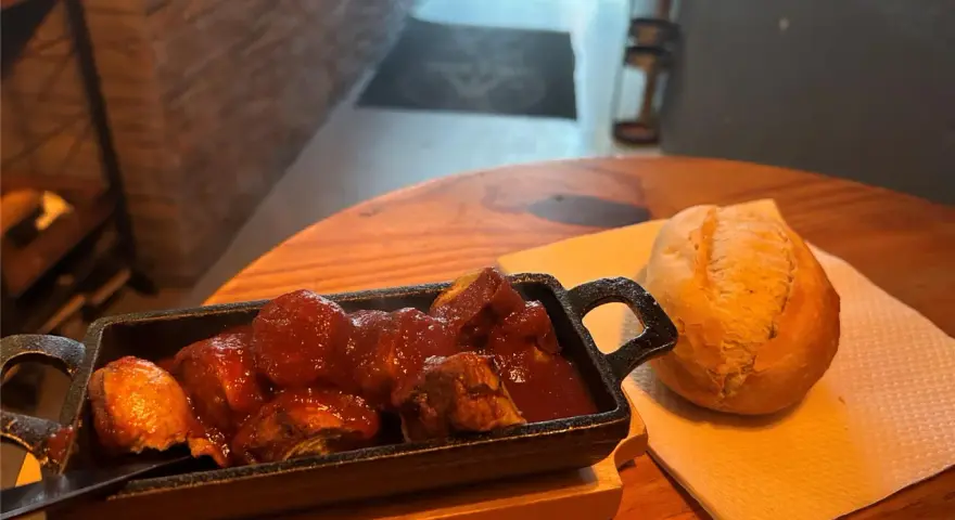 Herzhafte Steiger Wurst in Tomatensoße mit einem Brötchen auf einem Holztisch.