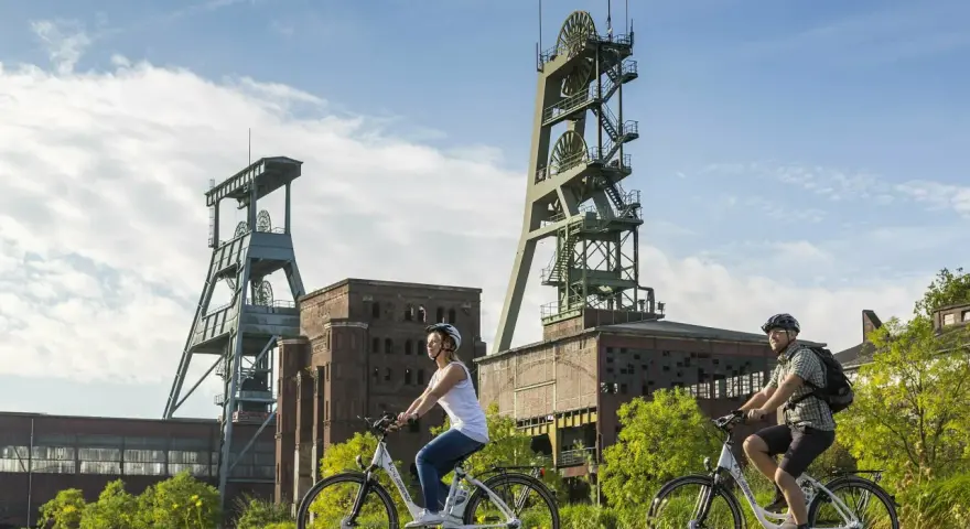 Ein Paar genießt eine Fahrradtour in Recklinghausen, vorbei an alten Fördertürmen und Industriegebäuden.